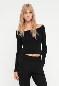 Fekete, bordázott, vállat szabadon hagyó crop top hosszú ujjakkal, puha, rugalmas anyagból készült. Magas derékú fekete nadrággal párosítva.