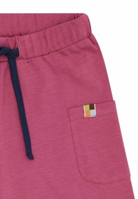 Rosafarbene Baumwollshorts mit einem elastischen Bund und einem navy-blauen Kordelzug, sowie einer Seitentasche, die mit einem mehrfarbigen Etikett verziert ist.