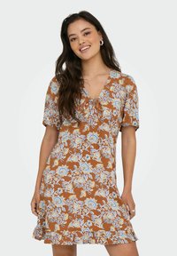 Bruine bloemenjurk met korte mouwen, een V-hals en een strikdetail. Beschikt over een rucheszoom en blauwe, gele en witte bloemmotieven.