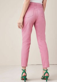Pantalons en denim rose à coupe slim, dotés de poches arrière, associés à des sandales à lanières vertes. Texture lisse avec un léger éclat.