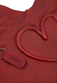 Sac fourre-tout en cuir rouge arborant un design de cœur en relief. Comprend une étiquette avec le nom de la marque "VENEZIA". Surface texturée et forme arrondie.