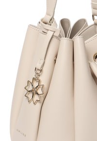 Borsa a secchiello in pelle beige con apertura raccorciata, dotata di un ciondolo floreale in tonalità oro. Texture liscia con accessori in oro.