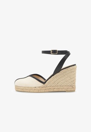 Espadrille compensée avec bout en toile beige, bride de cheville en cuir noir avec boucle dorée, et semelle plateforme en jute tressé.