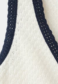 Gros plan d'un tissu tricoté blanc avec un motif texturé, bordé d'une bordure au crochet bleu marine le long d'un col en V.