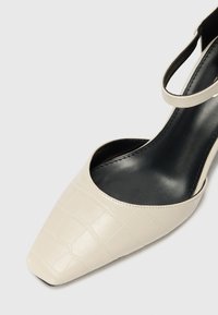 Beige krokodilkóngru í leðri með spitz útliti og ökkla band, með svörtu innri fóðri og sléttum yfirborði.