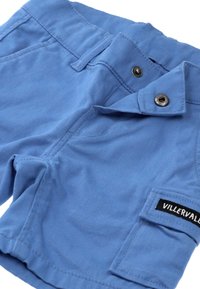 Vaaleansiniset puuvillahousut, joissa on napillinen vyötärö, sivutasku ja musta etiketti, jossa lukee "VILLERVALL." Sujuva pinta ja rento muotoilu.