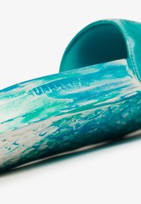Turquoise slide-on footwear featuring a textured upper and a glossy finish. The sole exhibits a patterned grip for traction.