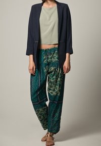 Marinblazer, ljusgrön crop top och mönstrade tealbyxor med elastisk midja och intrikata mönster. Brons sandaler kompletterar looken.