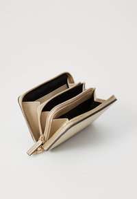 Beige bőr pénztárca strukturált felülettel, három rekesszel, arany cipzárral és fekete belső béléssel.