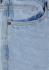 Světlé modré džíny s žlutým šitím a malým kovovým nýtem v horním rohu otvoru kapsy.