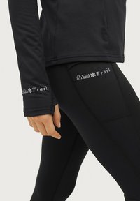 Zwarte sportieve lange mouwen top met een aansluitend ontwerp, voorzien van een logo op de manchette. Bijpassende zwarte leggings met een logo op de dij.