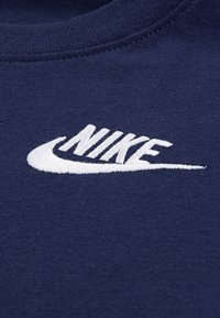 Tessuto di felpa blu navy con logo Nike bianco ricamato. Presenta una scollatura rotonda e un materiale morbido e testurizzato.