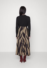 Lange braune Rock mit schwarzem Zebra-Streifenmuster, kombiniert mit einem langen schwarzen Oberteil und burgunderfarbenen Wildleder-Ankle-Boots.