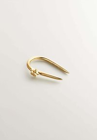 Broche en tono dorado con forma de U curva, extremos puntiagudos y un acento escultórico en el centro. Superficie lisa con un acabado reflectante.