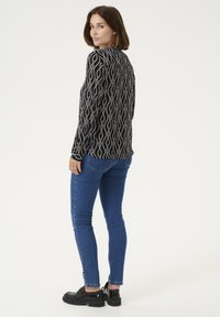 Maglietta a maniche lunghe bianca e nera con motivo geometrici, jeans aderenti blu e scarpe chunky nere. La maglietta presenta un design geometrico e un collo rotondo.
