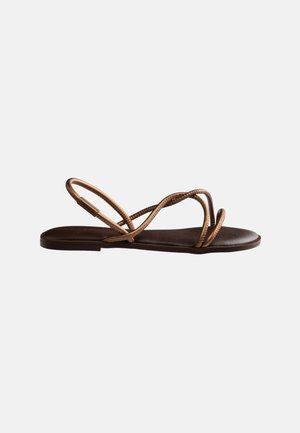 Sandale plate marron foncé avec de fines lanières métalliques bronze traversant le pied et une bride arrière pour le maintien.