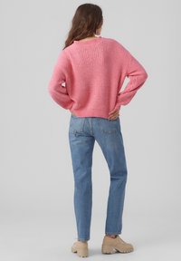 Rosa Strickpullover mit strukturiertem Muster, lockere Passform und langen Ärmeln, kombiniert mit blauen gerade geschnittenen Denimjeans und beigen Plateauschuhen.