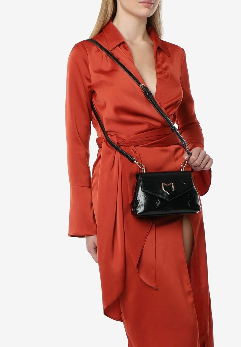 Sort patentlæder håndtaske med et guld hjerteformet accent, udstyret med en crossbody rem. Båret med en lys orange satin kjole.