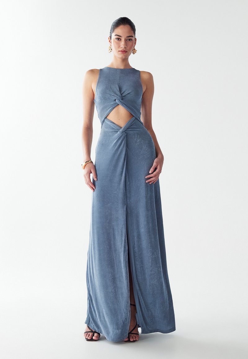 Ilga, be rankovių, mėlyna aksominė suknelė su priekine išpjova ir sukimo detaliu. Tiesus siluetas su aukšta skl automate, derinamas su juodais diržais sandalais.