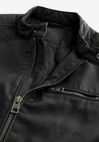 Chaqueta de cuero negra con forro acolchado, cuello alzado y cremalleras plateadas en el frontal y en el bolsillo del pecho. Textura suave.