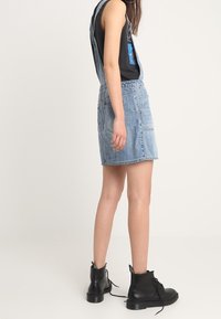 Jeansoverallklänning i ljusblått med justerbara axelband, två framfickor och rak fåll, kombinerad med svarta snörkängor.