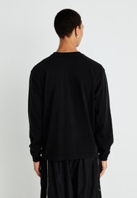 Camiseta de manga larga negra hecha de tela suave, con escote redondo y corte relajado. La vista trasera muestra un diseño simple sin detalles gráficos.
