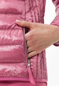 Chaqueta acolchada rosa con acabado brillante, que incluye un bolsillo con cremallera lateral y un logo cerca del dobladillo. La tela presenta un diseño acolchado.