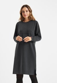 Zwarte sweatshirt jurk van een zachte stof, met een ronde halslijn, lange mouwen en zijsplitten voor gemakkelijke beweging. Subtiele branding.