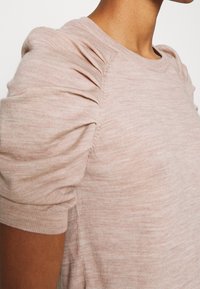 Lichtroze gebreide trui met korte pofmouwen, een ronde halslijn en een zachte, gestructureerde afwerking. Gedetailleerd met subtiele strepen.