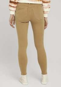 Jeans de corte slim, en color beige con una textura suave, que presentan dos bolsillos traseros y una cintura alta, combinados con zapatillas blancas.