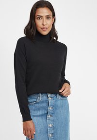 Schwarzer gestrickter Rollkragenpullover mit strukturiertem Muster, kombiniert mit einem blauen Denim-Bleistiftrock mit knopffront.