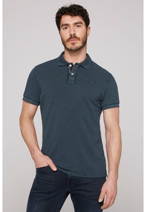 Donkerblauwe polo, korte mouwen, kraag met drie knopen, subtiele textuur, geborduurd logo op de borst, gecombineerd met donkere jeans.