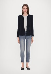 Sötétkék, illeszkedő zakó plisszírozott elemekkel, világosszürke toppal és világoskék skinny farmernadrággal párosítva. Fekete balerina cipő egészíti ki a megjelenést.