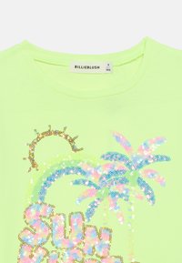 Νεον πράσινο μπλουζάκι με σχέδιο διακοσμημένο με παγιέτες που απεικονίζει ήλιο και φοίνικες, με ετικέτα "BILLIEBLUSH." Στρογγυλή λαιμόκοψη, κοντά μανίκια.