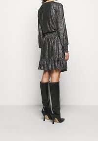 Robe noire à sequins avec un ourlet à volants, des manches longues et une taille froncée. Associée à des bottes noires à talons montant jusqu'aux genoux.