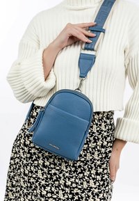 Small blue leather crossbody bag with a textured finish, silver hardware, and an adjustable striped strap. Coin pocket and logo detail.