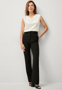 Schwarze ausgestellte Hosen kombiniert mit einem cremefarbenen ärmellosen Oberteil mit einem drapierten Ausschnitt. Der Look wird mit schwarzen Sandalen mit Absatz abgerundet.