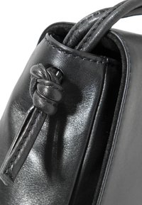 Borsa a tracolla in pelle nera con una texture liscia. Presenta un dettaglio con una tracolla annodata e un design strutturato, che mette in evidenza le cuciture lungo i bordi.
