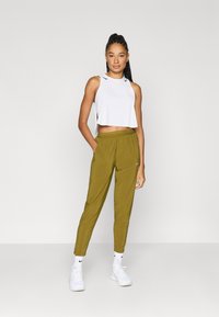 Λευκό τοπ χωρίς μανίκια με κοψίματα στους ώμους, σετ με παντελόνια σε ελιά πράσινο χρώμα με στενή γραμμή και λευκά αθλητικά παπούτσια με μαύρες λεπτομέρειες.