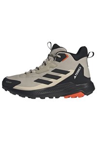 Chaussure de randonnée mi-haute beige avec des accents noirs et oranges ; présente une tige en synthétique texturé, une semelle en caoutchouc et trois bandes noires sur le côté.