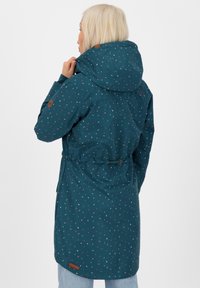 Giacca impermeabile turchese con cappuccio, decorata con un motivo di piccoli punti colorati, vita elasticizzata e una patch con logo vicino all'orlo.