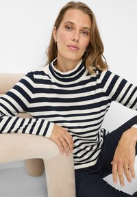 Gestreepte coltrui in marineblauw en crème, met een aansluitend ontwerp, geribbelde textuur en lange mouwen, gecombineerd met donkere broek.