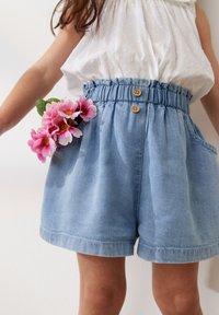 Shorts in denim leggero blu con vita elastica, due tasche e bottoni in legno. Fiori rosa sono riposti nella tasca destra.