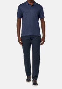 Námořnická polo košile s krátkými rukávy, plochým límcem; v kombinaci s tmavými kalhotami a černými teniskami. Směs bavlny, hladká textura.