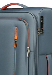 Valigia blu con tessuto strutturato, dettagli arancioni, doppie cerniere e serratura a combinazione. Presenta una maniglia arrotondata sulla parte superiore.