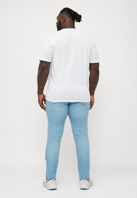 Camiseta blanca de manga corta combinada con jeans slim-fit de color azul claro. Los jeans tienen un ligero desgastado en los bolsillos traseros.