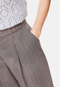 Gray herringbone pants with a flat front, tailored fit, and side pockets, paired with a light knit top. Texture visible in fabric.
