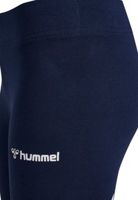 Leggings blu navy con una texture liscia, caratterizzati da un logo bianco sulla parte inferiore della gamba. Il design include una semplice vita cucita.
