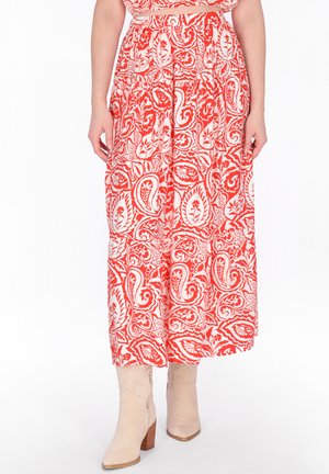 Fließender knöchellanger Rock mit rotem und weißem Paisley-Muster, kombiniert mit beigen Stiefeletten mit Absatz an einer stehenden Person.