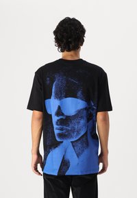 Black cotton t-shirt featuring a large blue graphic of a face with sunglasses on the back. Short sleeves and relaxed fit.